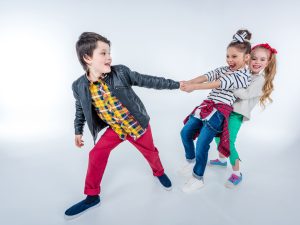 side view of laughing girls pulling up boy isolated on grey