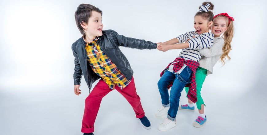side view of laughing girls pulling up boy isolated on grey