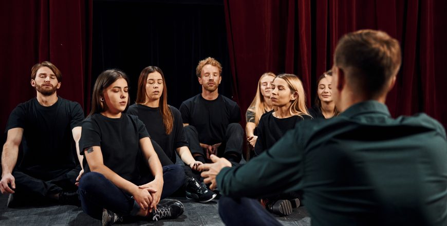 Sitting on the floor. Group of actors in dark colored clothes on rehearsal in the theater